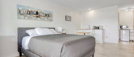 Un dormitorio moderno con una cama grande, un escritorio y una kitchenette.