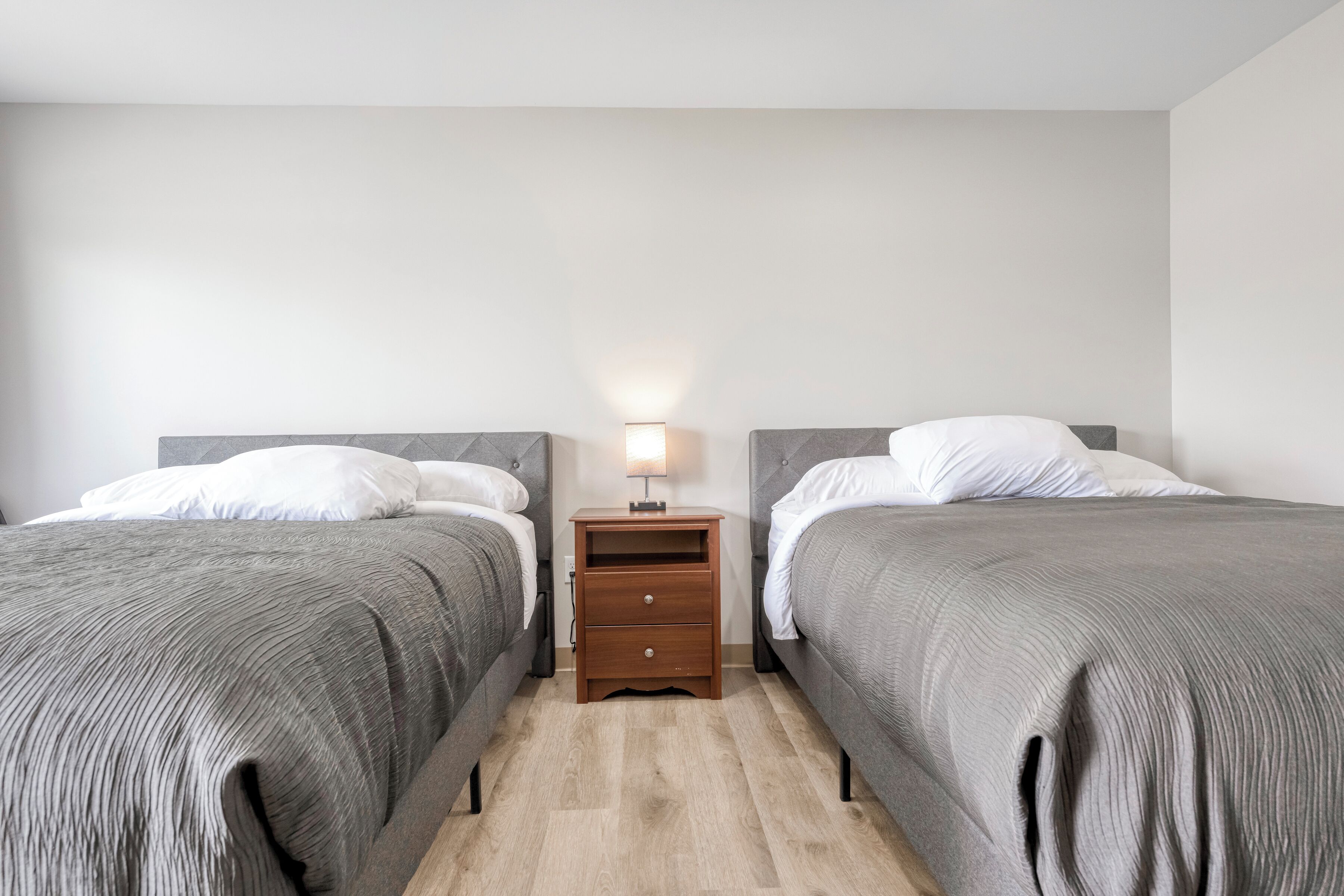 Habitación doble con dos camas, una mesita de noche con lámpara y suelo de madera.