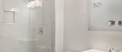 A bathroom with a glass-enclosed shower, a toilet, and a sink with a mirror above it.