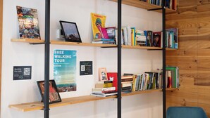 A bookshelf with books and a framed picture, a poster for a free walking tour, and a QR code. - The Central House Barcelona Gracia - Hostel (Barcelona)