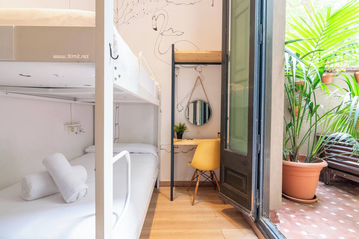A compact room with a bunk bed, a desk with a chair, a round mirror, and a potted plant.