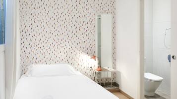 Una habitación de hotel con una cama bien hecha, un escritorio pequeño con una lámpara, un espejo y un inodoro.