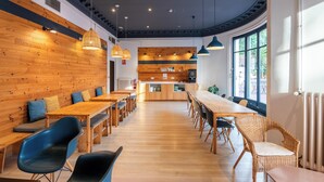 A modern dining area with wooden walls, a long table, and blue chairs. - The Central House Barcelona Gracia - Hostel (Barcelona)