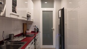 A narrow kitchen with white cabinets, a red countertop, and a stainless steel sink. - The Central House Barcelona Gracia - Hostel (Barcelona)