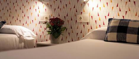 A hotel room with a patterned wallpaper, a bedside table with a potted plant, and a checkered pillow.