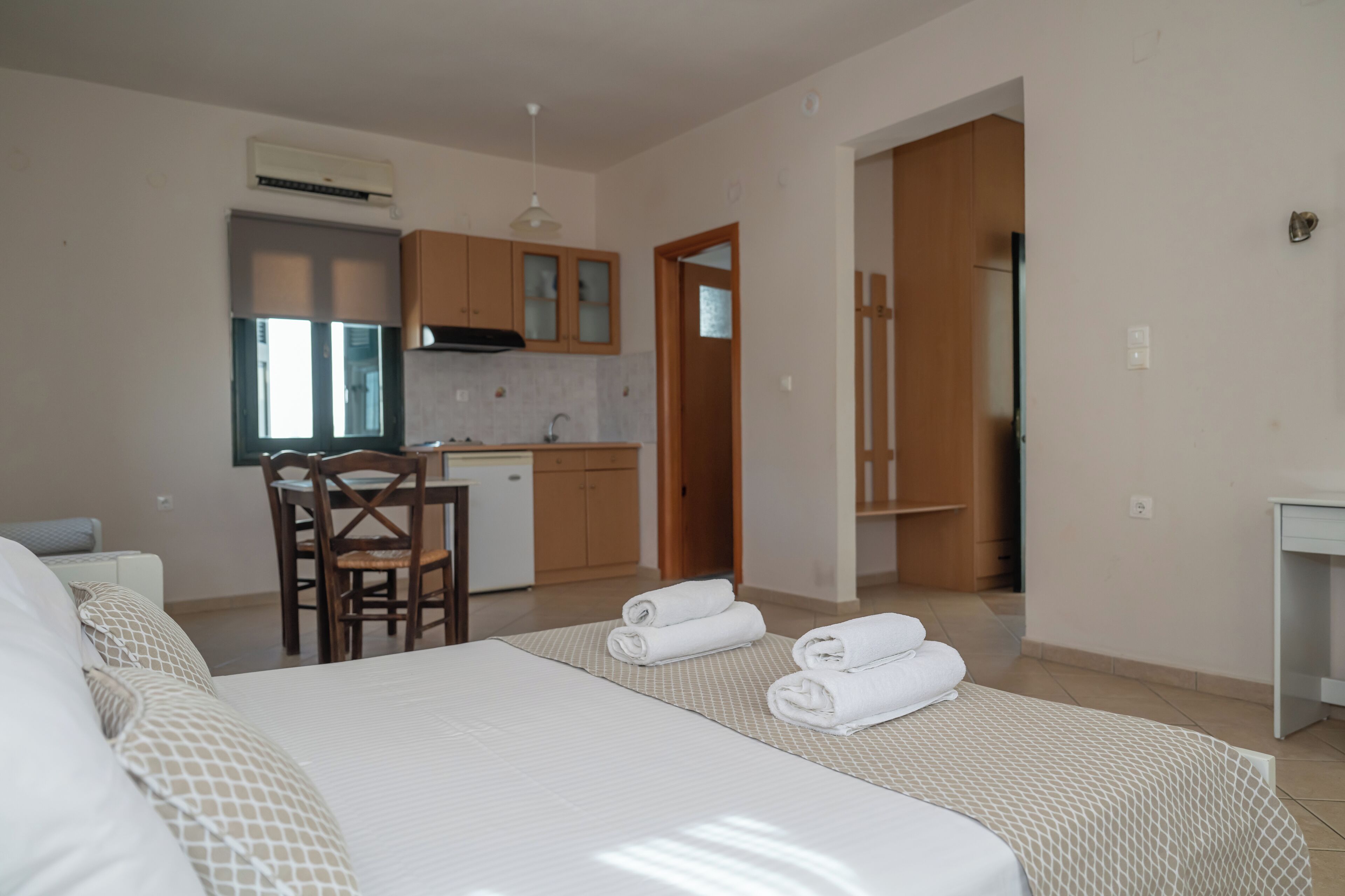 A hotel room with a bed, a desk, a chair, a kitchenette, and a bathroom.