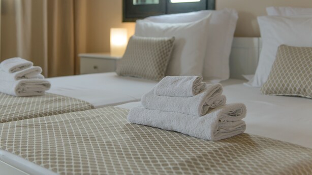 Ein Hotelzimmer mit zwei Betten, jedes mit einem ordentlich gefalteten Handtuch, einer gemusterten Tagesdecke und einem Kopfkissen.