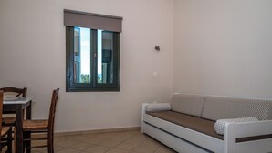 Ein Zimmer mit einer Couch, einem Esstisch mit Stühlen und einem Fenster mit Jalousien.