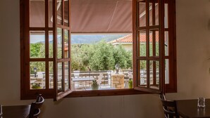 Ein Zimmer mit großem Fenster, das einen Balkon mit Gartenmöbeln und Blick auf Grünflächen und Berge zeigt.
