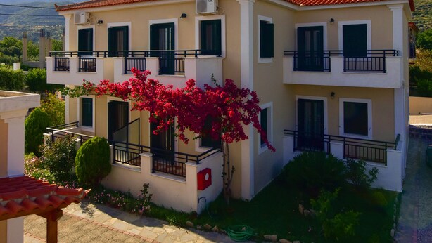 A two-story building with balconies, a tiled roof, and a garden with flowering plants.