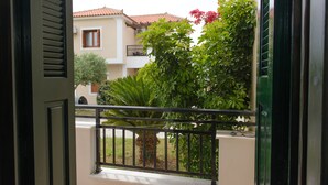 A view from a balcony with a metal railing, a palm tree, and a building with a red-tiled roof in the background.