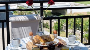 Ein Balkon mit einem Tisch, Frühstücksgebäck, einer Rosenvase und einer malerischen Hügellandschaft.