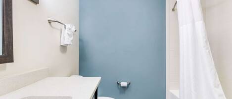 Une salle de bain équipée de toilettes, d’un porte-serviettes, d’un rideau de douche et d’un lavabo.
