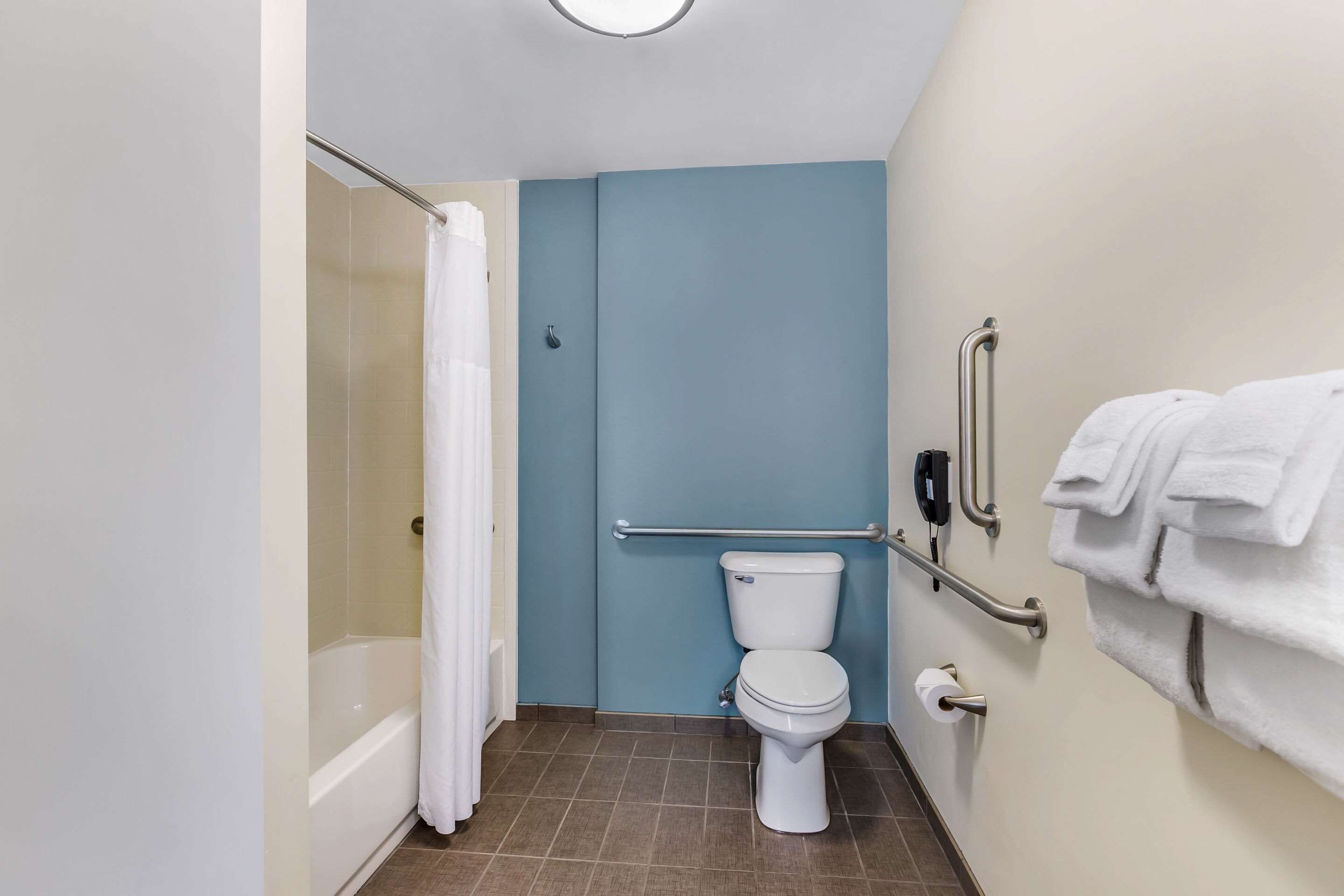 Un baño con bañera, inodoro y barras de apoyo.