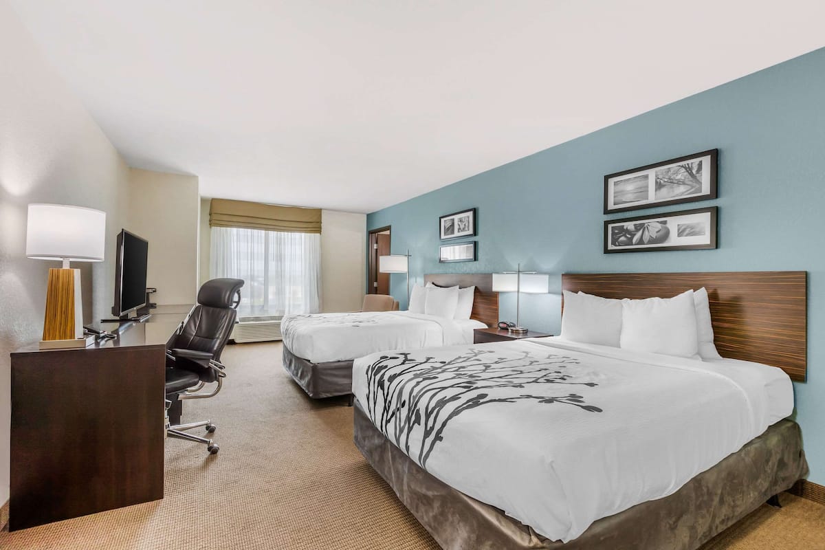 A hotel room with two beds, a desk, a chair, and a television.