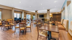 A spacious hotel dining area with multiple tables and chairs, a flat-screen TV mounted on the wall, and a large window providing a view of the cityscape. - Sleep Inn & Suites Ames near ISU Campus (Ames)