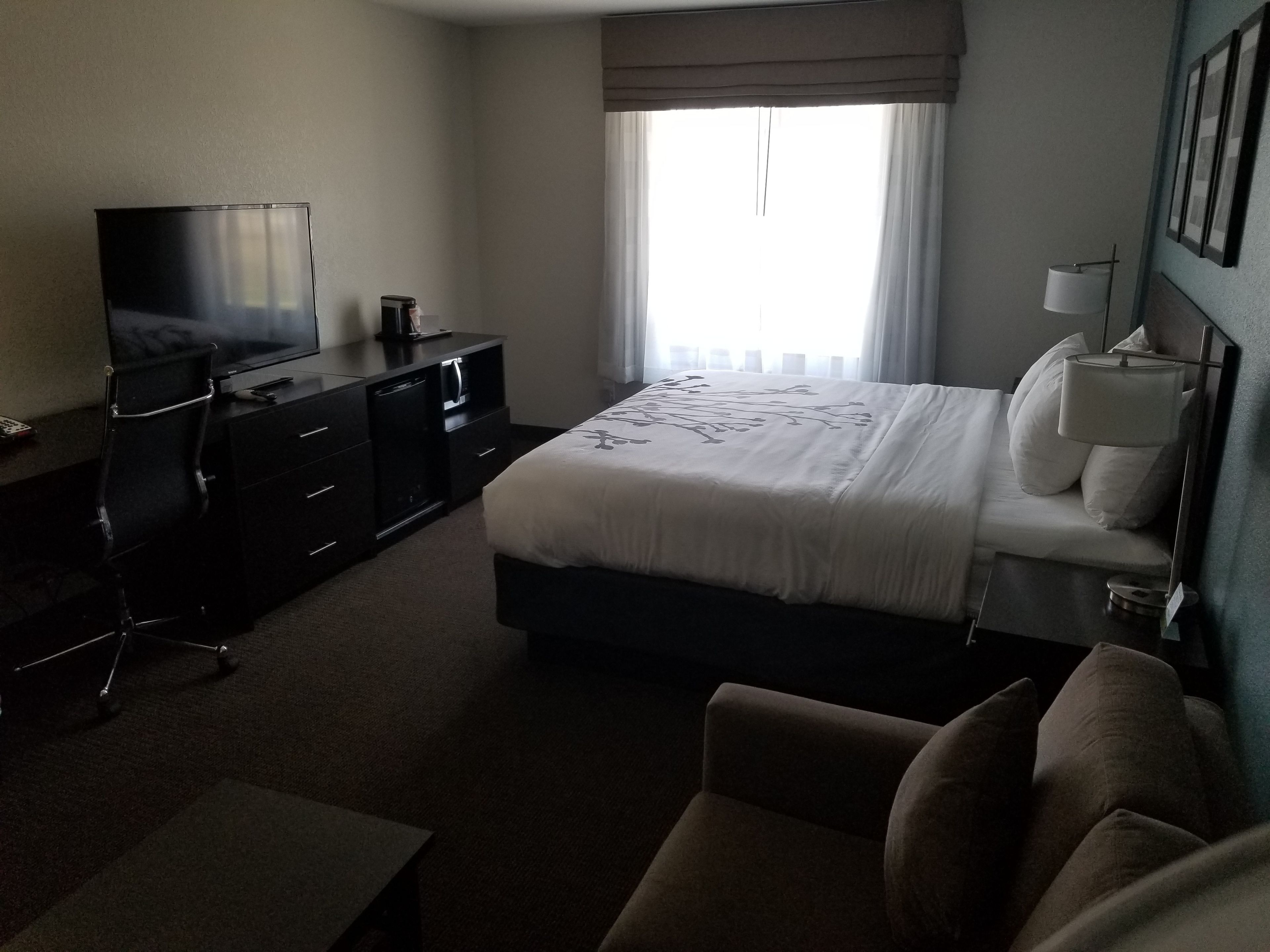 A hotel room with a bed, a TV, a desk, and a chair.