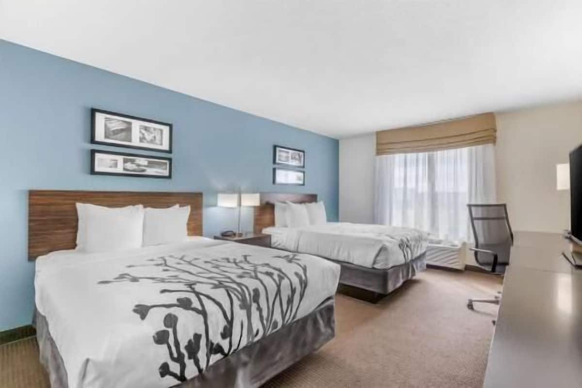 A hotel room with two beds, a desk, a chair, and a TV.