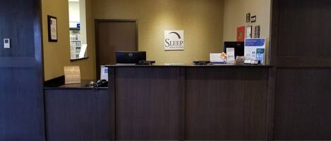 En receptionsdisk med en skylt för Sleep Inn & Suites, en dator och informationsbroschyrer.