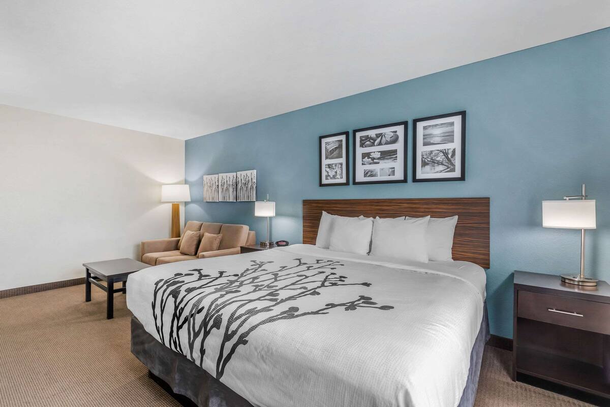 A hotel room with a large bed, a nightstand, a chair, and wall art.