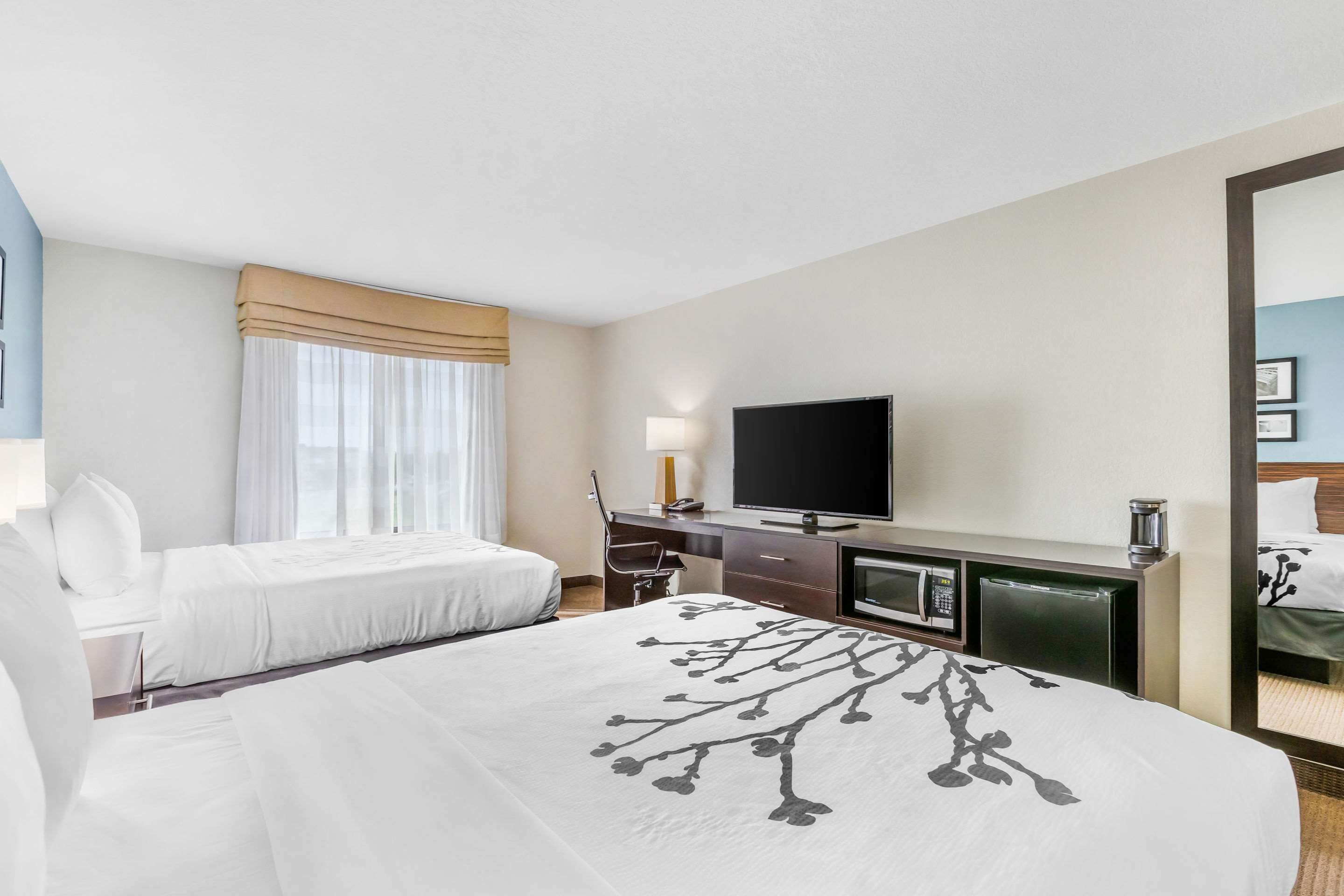 A hotel room with a large bed, a smaller bed, a desk with a television, and a mirror.