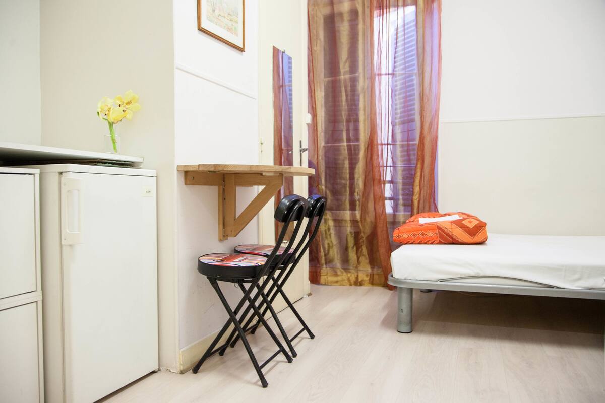 A small room with a bed, a desk, a chair, and a refrigerator.