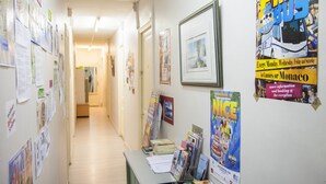 Un pasillo con carteles y avisos en las paredes, un mostrador de recepción con folletos y un cuadro enmarcado.