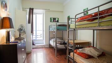 Une chambre de dortoir avec des lits superposés, un bureau, une lampe, un ventilateur et une fenêtre avec un rideau.
