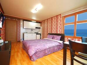 Quarto compacto com cama, pequena escrivaninha e vista para o mar pela janela.