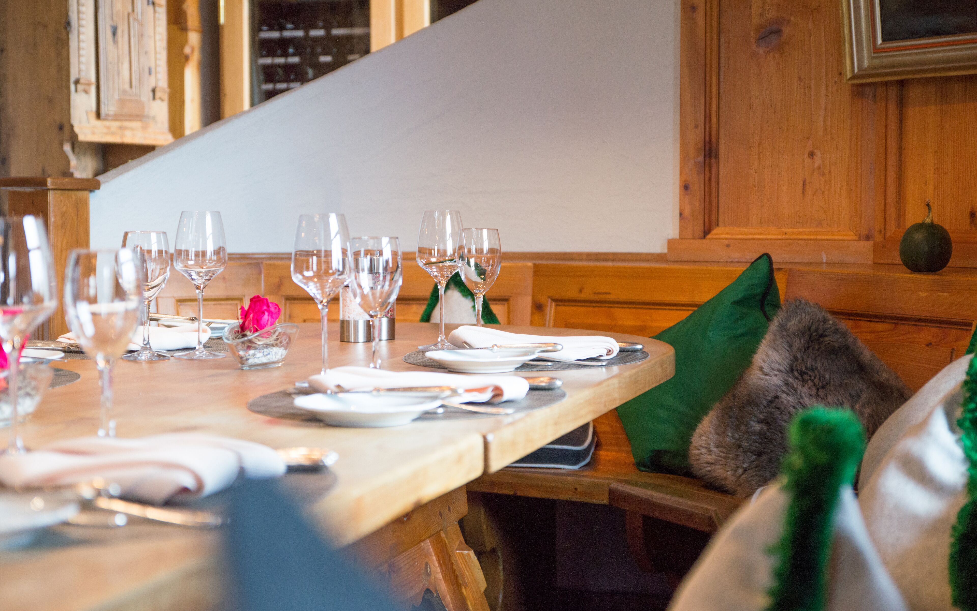 A dining table set with wine glasses, plates, and cutlery, with a green cushion on the bench.