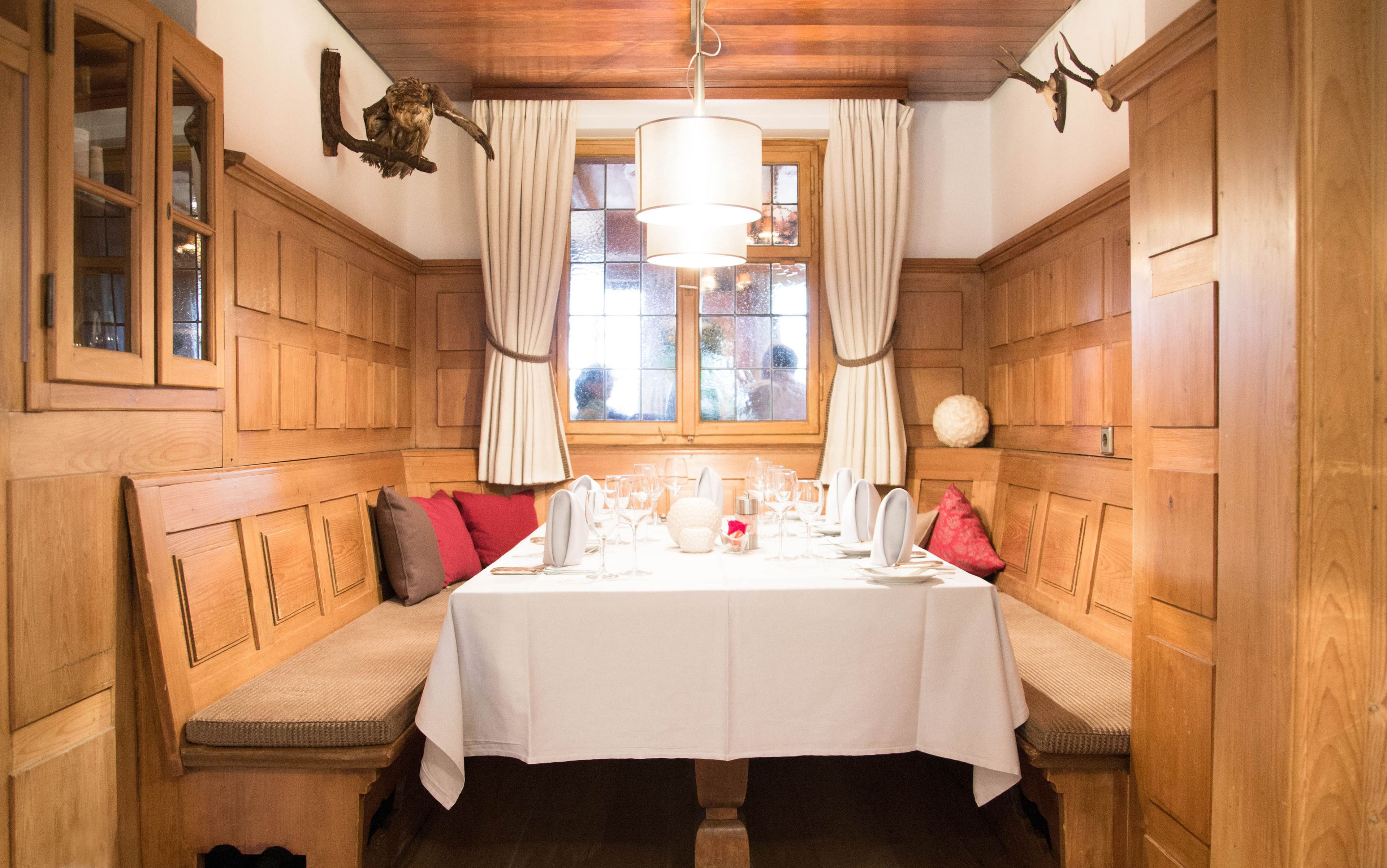 Comedor con mesa de madera dispuesta para cuatro personas, flanqueada por bancos de madera con cojines.
