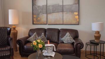 A living room with a brown leather sofa, two leopard print pillows, a vase with flowers, and a small table with a lamp.