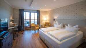 A hotel room with a large bed, two bedside tables, a desk with a chair, a TV, and a window with curtains.