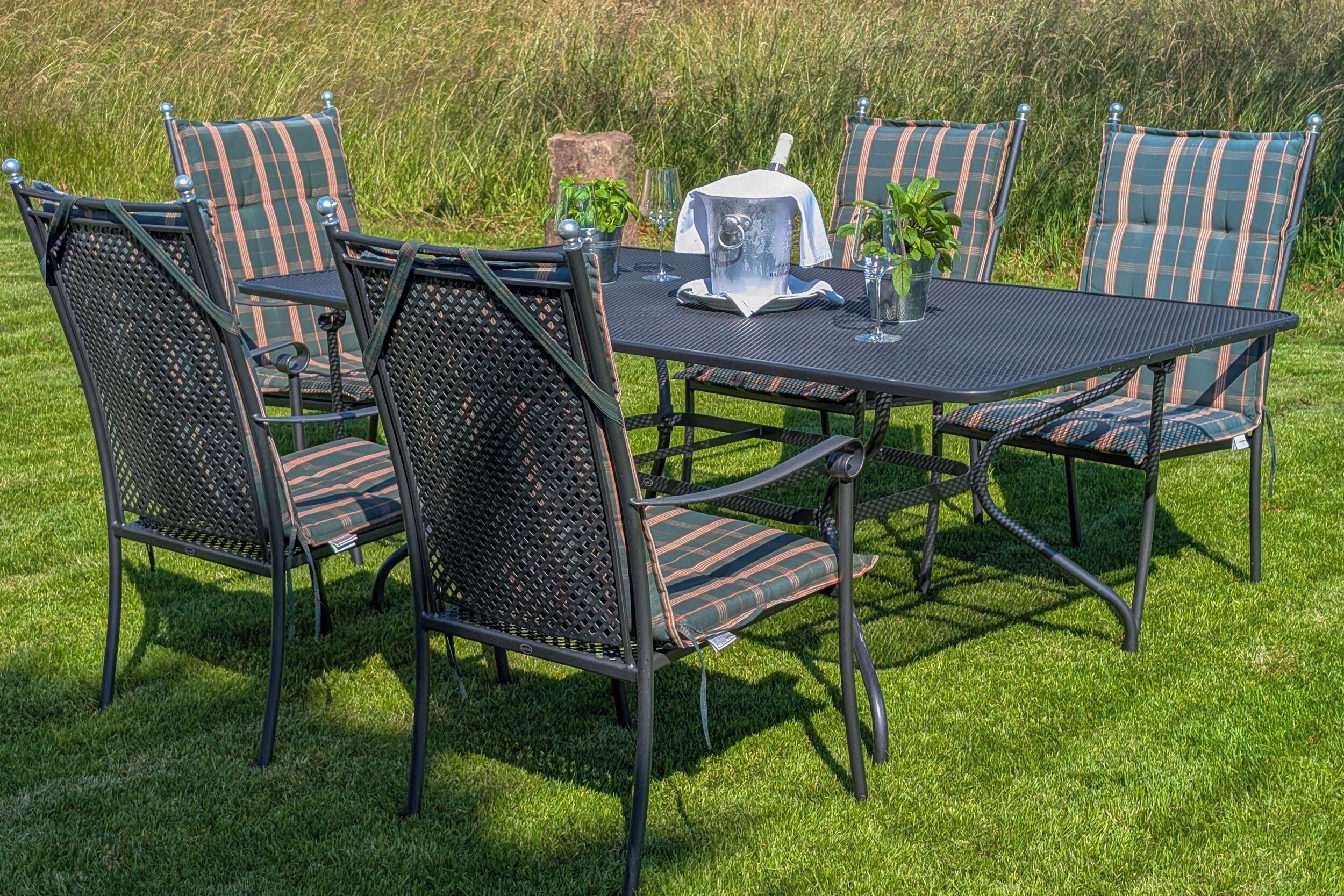Une table ronde entourée de chaises, une carafe et un verre posés sur une pelouse.