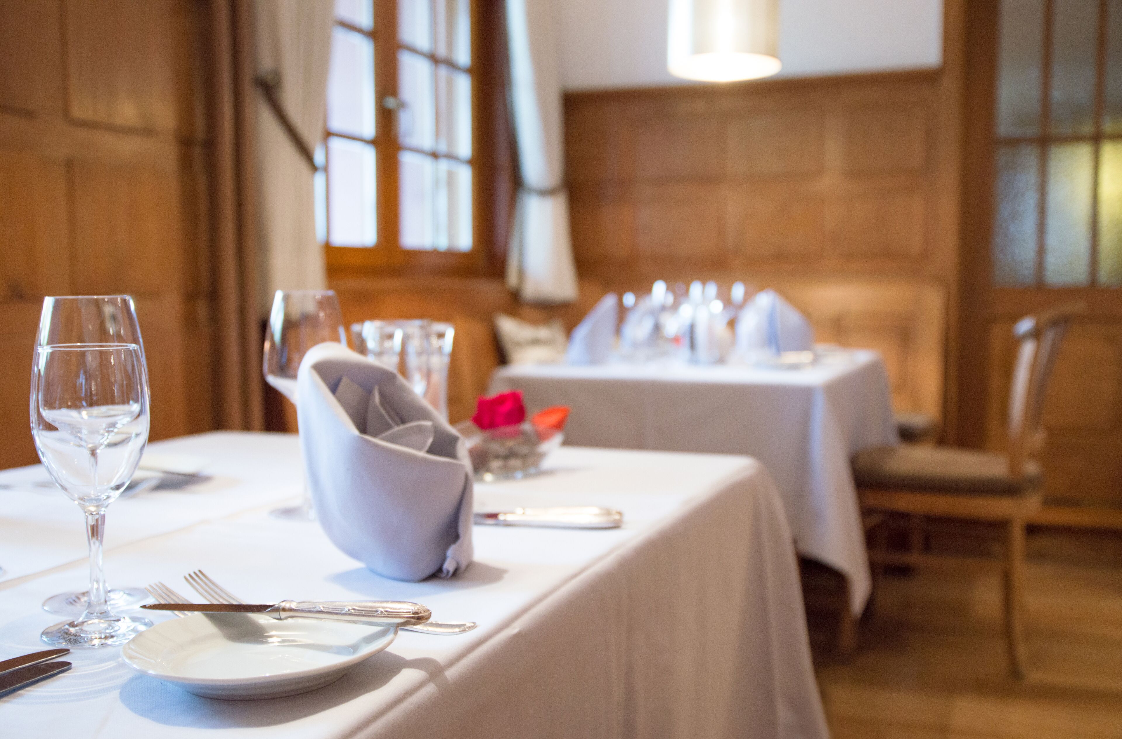 Een eettafel gedekt met witte tafelkleden, bestek en een glas water.