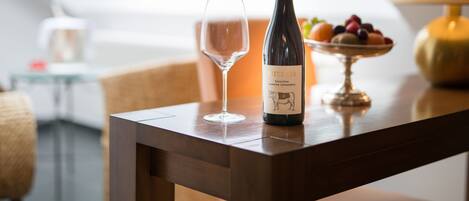 A bottle of Metzger wine, a glass, and a bowl of fruit on a wooden table in a modern room with a skylight.