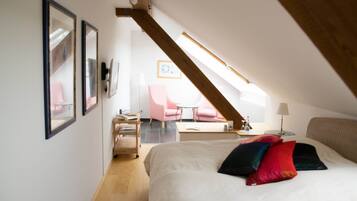 A bedroom with a large bed, a desk, a chair, and a small table. There is a window with a view of a pink chair and a table outside.
