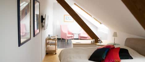 Un dormitorio con una cama grande, un escritorio, una silla y una mesita. Se ve una ventana con vistas a una silla y una mesa afuera.