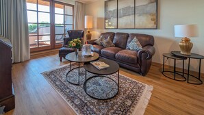 A living room with a brown leather sofa, two coffee tables, a rug, and a large abstract painting on the wall.