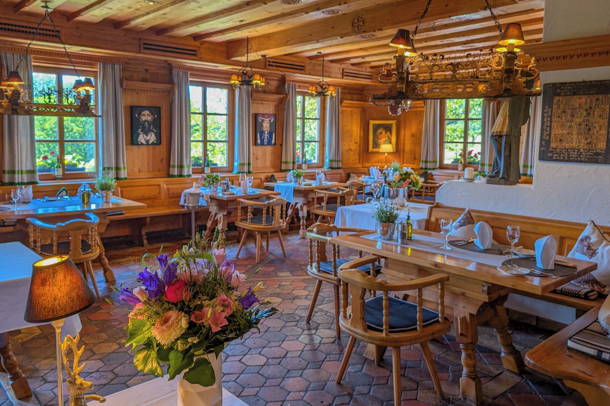 Un interior rústico de madera con varias mesas y bancos para comer, amplias ventanas con cortinas, y una variedad de adornos en las paredes.