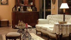 Een klassieke woonkamer met een witte bank, een houten kast, een klein tafeltje met een roze kaars en een kant kleed.