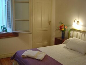 Une chambre d’hôtel avec un lit, une table de chevet ornée d’un vase de fleurs et une fenêtre avec des stores.