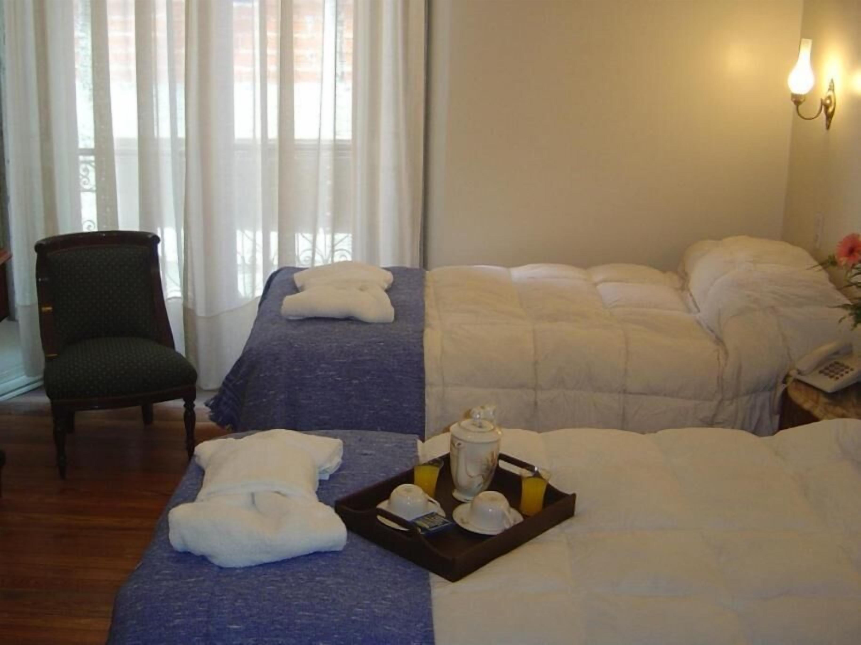 A hotel room with two beds, a chair, and a tray with toiletries.