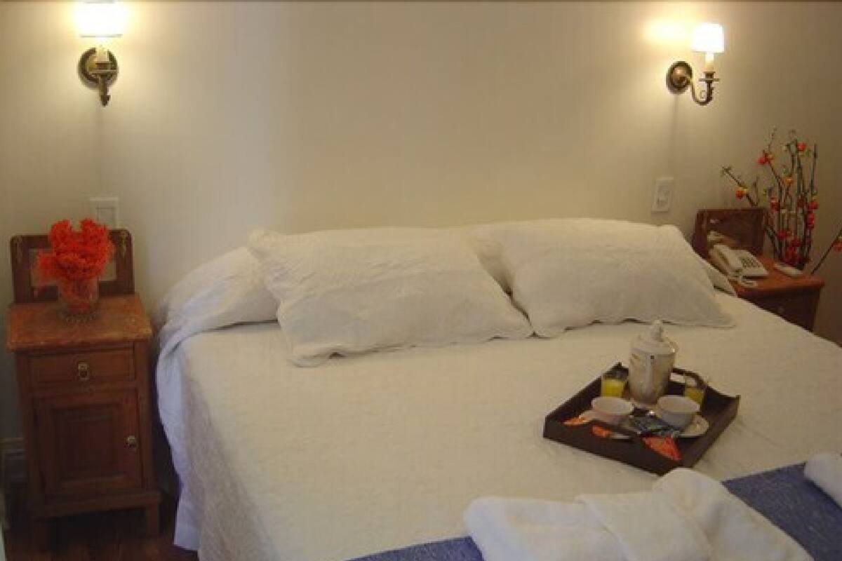 Ein ordentlich bezogenes Bett mit weißen Leinen, ein Nachttisch mit Lampe und ein Tablett mit Frühstücksgebäck.