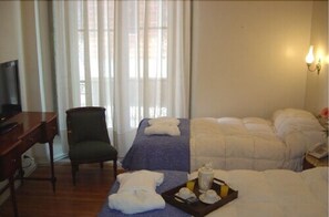 Une chambre d’hôtel avec un lit, une chaise, un bureau et une fenêtre avec des rideaux.