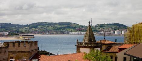 A coastal cityscape with historical architecture, including a prominent church tower and a waterfront promenade.