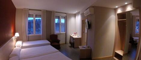 A hotel room with two beds, a desk, a chair, a small table with a vase, and a mirror.