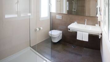 Ein modernes Badezimmer mit Duschkabine aus Glas, einer weißen Toilette und einem Waschbecken mit Spiegel darüber.