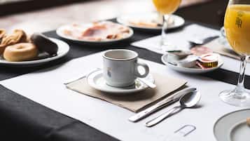 A breakfast setting with a cup, spoon, and fork on a table, accompanied by plates of food and a glass of orange juice.