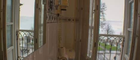 A bathroom with a toilet, a sink, and a mirror. There is a window with a view of a street and trees.
